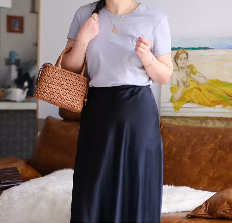 Woman wearing a straw hat and holding a woven bag in a room with a painting on the wall.