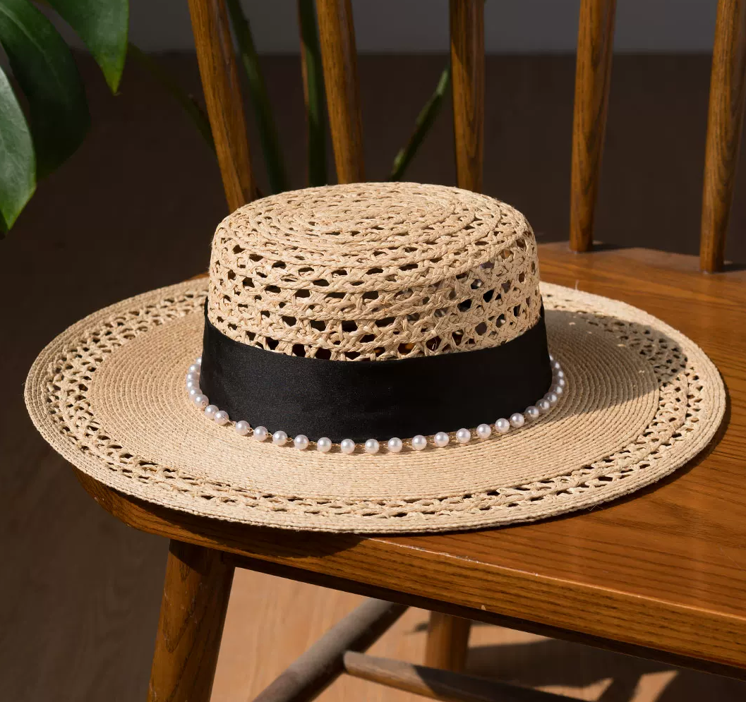 Woven straw hat with a black band and pearl embellishments on a wooden chair.