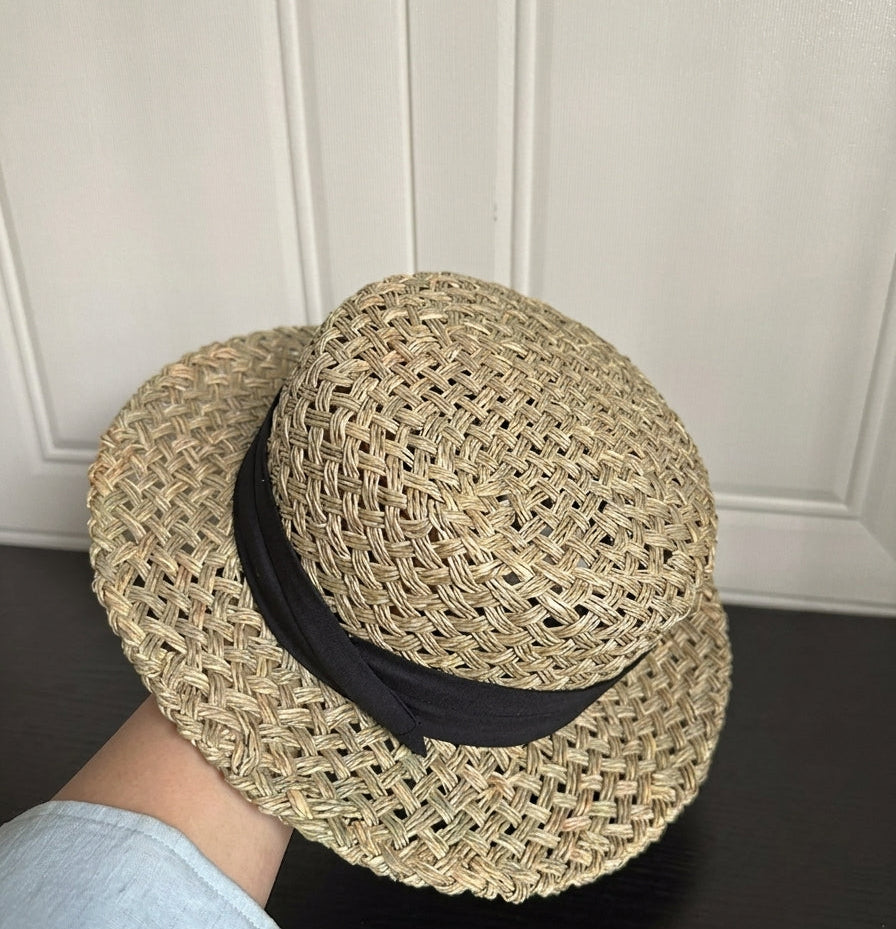 Woven straw hat with a black band held by a person against a white paneled wall.